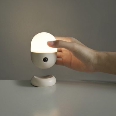 A hand-focused image of a lit, oblong and spheroid-shaped lamp held by a person
