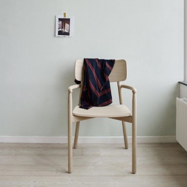 SKAGERAK Hven Arm Chair, Oak in a room with a small picture hanging on the wall