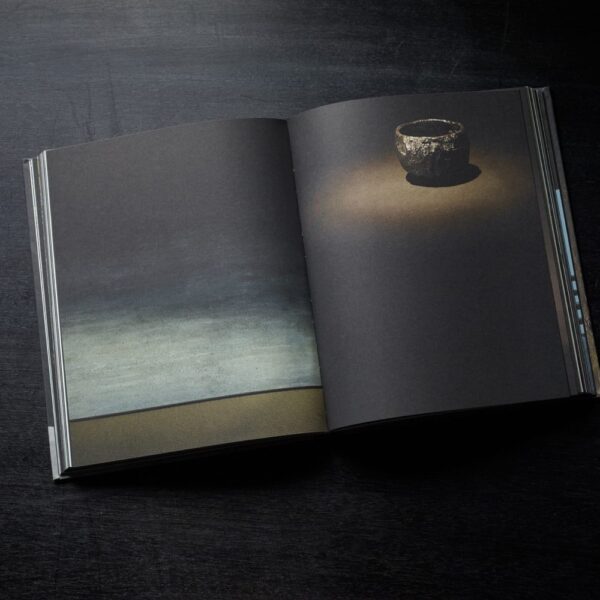 A excerpt from Axel Vervoordt's Wabi Inspirations Coffee Table Book featuring a dimly-lit jar placed in the ground.