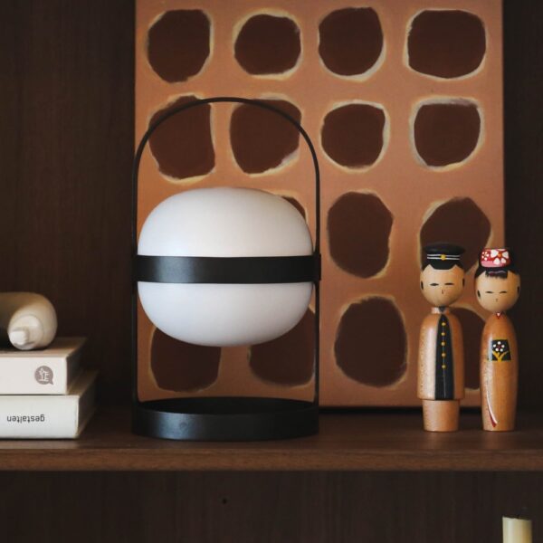 A spherical shaped lamp with a arch-shaped handle placed to a shelf next to books and small objects.