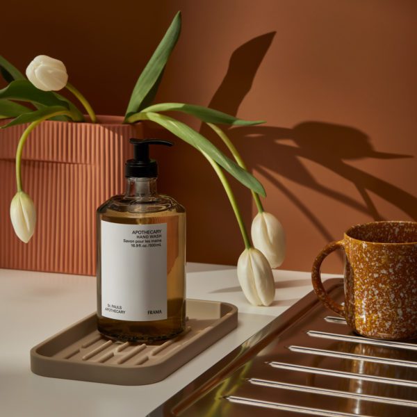 Large, amber soap bottle on a brown sink tray with tulips in the background