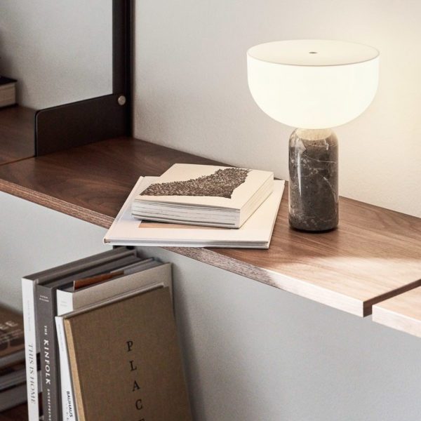 NEW WORKS' Kizu Table Lamp illuminating a bookshelf it is sat atop of