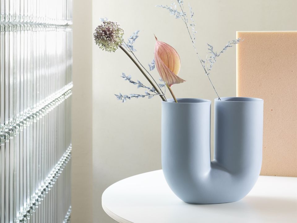 MUUTO's Kink Vase in a soft baby blue. styled on a table with flowers/
