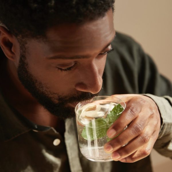 A person sipping a glassful of water with lime and garnish
