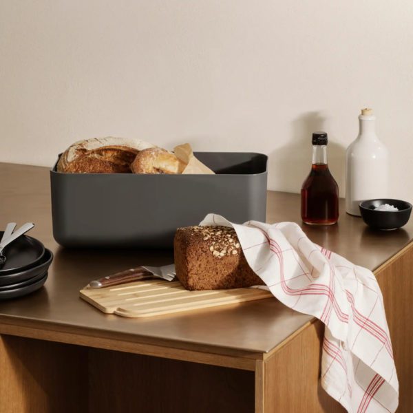 A rectangular-shaped container with bread inside placed in a wooden table with condiments and a hand towel.