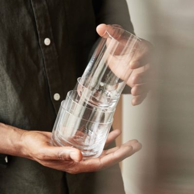A person holding a stack of four crystal clear glasses