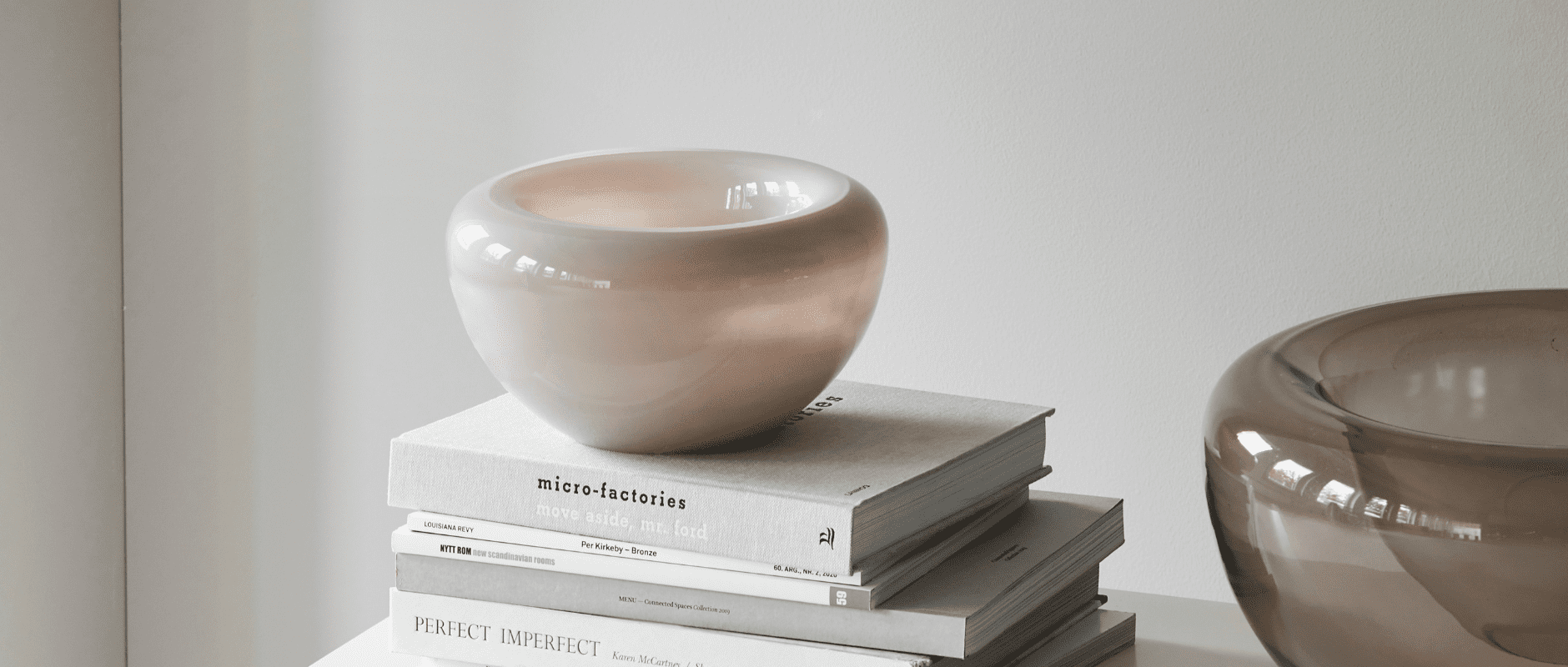 A photo of the Kristina Dam Studio Opal Bowl in Beige, placed on top of a stack of books.