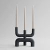 Black three pronged candelabra with three neutral coloured candles held inside each opening