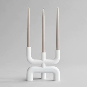 Studio photography of a white three pronged candelabra displayed with three neutral coloured tapered candles