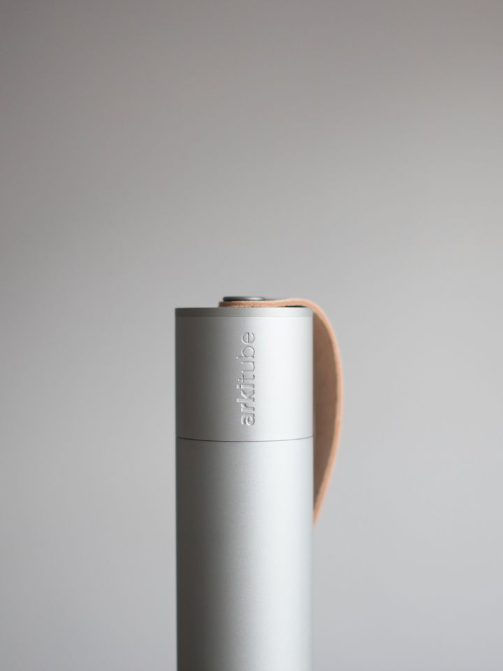 This is a shot of the Arkitube Document Holder, designed by PerCapita and shot by Wei Xiong Yap. It's a cylindrical design in a slivery grey finish. It has a cognac leather brown strap at the top, and engraved in the lid is the word "arkitube".