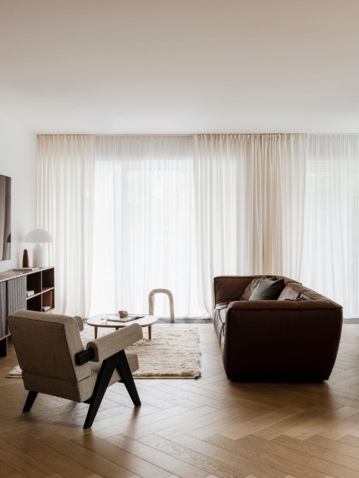 An interior photo of Botaniczna Apartment by Agnieszka Owsiany Studio. The features a herringbone patterned timber floor, sheer curtains, and contemporary furnishings. 