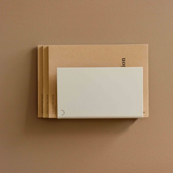 Natural light, perspective view of a beige, wall-mounted magazine holder.