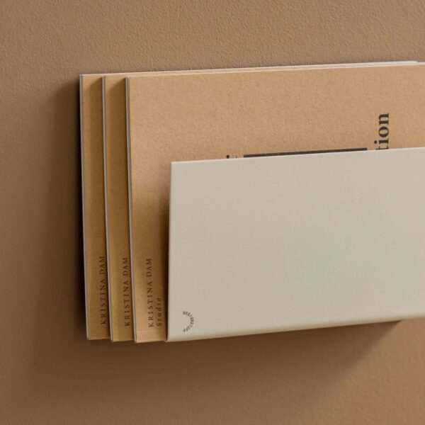 Natural light, close up, perspective view of a beige, wall-mounted magazine holder.