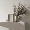 Dried leaves in Serene flowerpot sand and Sculpture candle holder by Kristina Dam Studio on a concrete shelf