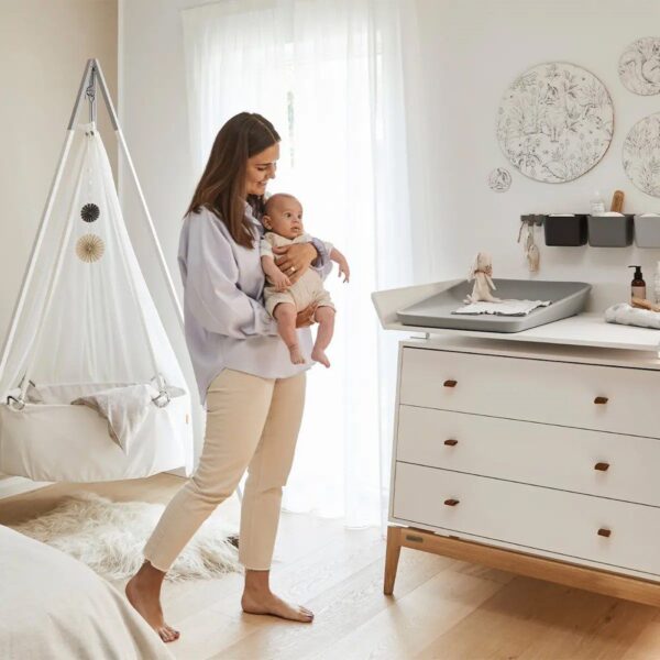Natural light, perspective view of a mother carrying her child next to a white cabinet with a 3-piece grey organiser mounted above it.