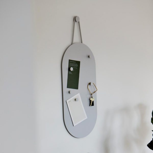 A grey, oblong-shaped, key-laden bulletin board hanging on a round hook.