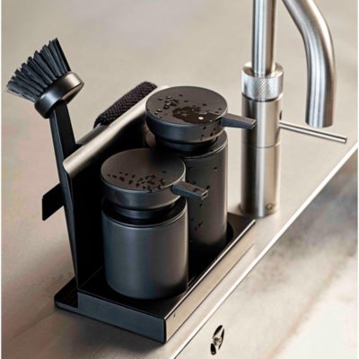 Cropped shot, natural light, isometric view of a stainless steel kitchen sink with a black-coloured tray of cleaning tools beside the sink's faucet.
