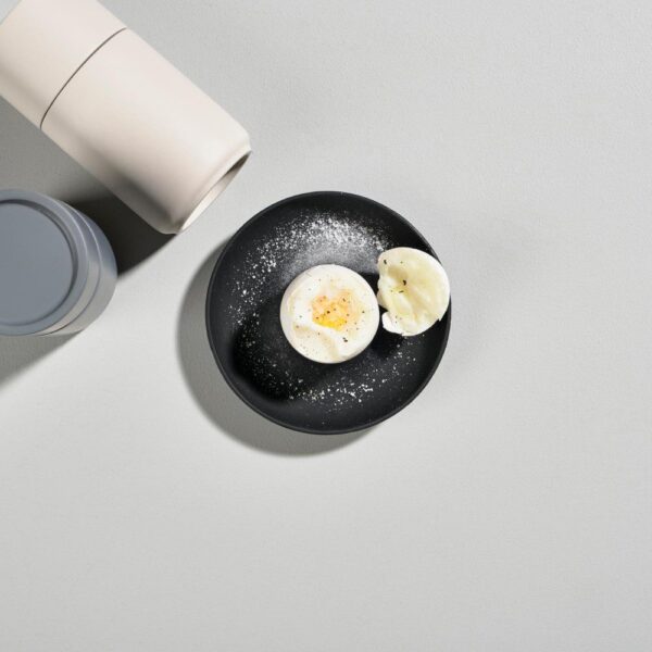 Top view of a half-sliced hard boiled egg perched on an egg cup and garnished with salt and herbs.