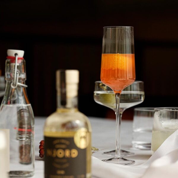 Perspective view of a champagne glass placed in the center of a table along with two bottles of spirit and a cocktail glass in the foreground.