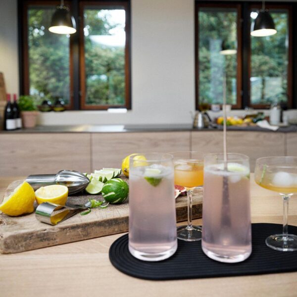 Kitchen table scene with two cocktail drinks as subjects and a chopping board with citrus fruits and a used channel knife laid down.