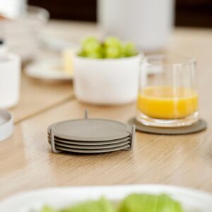Kitchen table scene with a glass of orange juice atop a coaster and a stack of four, light brown coasters