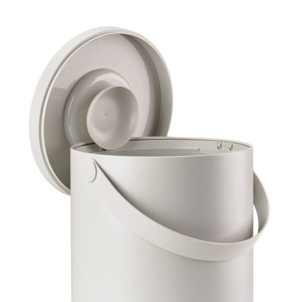 White background, studio image of a grey, cylindrical trash bin with a pail-type handle with its cover perched on the rim of the bin.