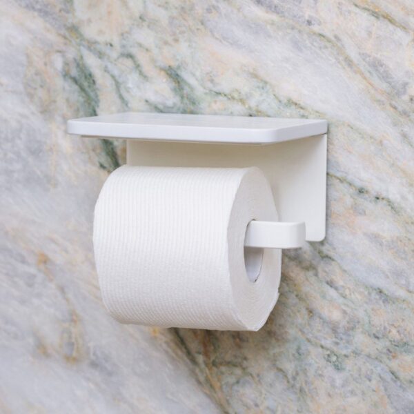 Perspective view of a white-coloured, wooden toilet roll holder with one roll of toilet paper attached, mounted on a white, streaked marble wall.