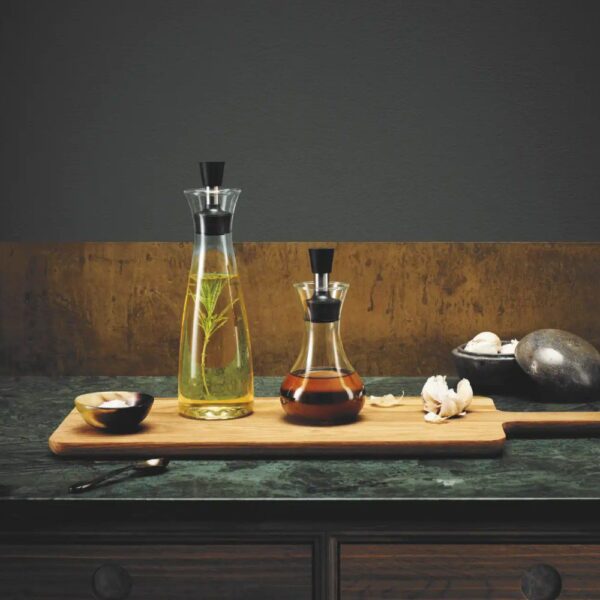 Dark background, studio image, editorial style, perspective view of two, clear dressing shaker containers placed on top of a chopping board with cloves of garlic next to them.
