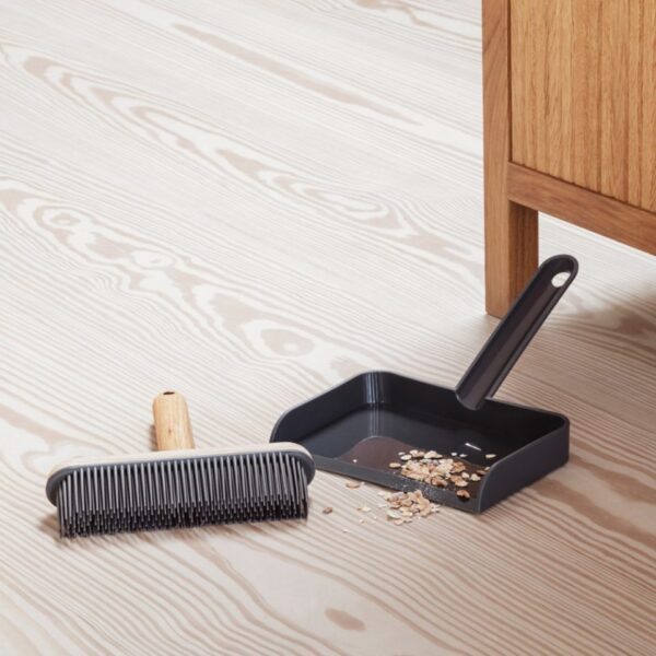 Natural lighting, cropped, perspective of a static brush set and dustpan gathering oatmeal off the floor.