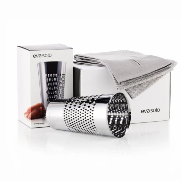 White background, studio lighting, perspective view of a stainless steel, canister-shaped grating bucket with boxes and a towel behind it.