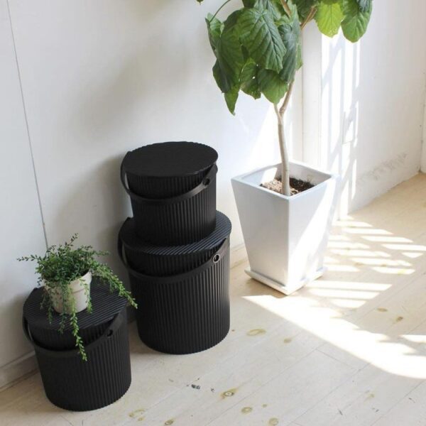 Natural light, perspective view of 3 black, different-sized storage bins placed next to a white flowerpot.
