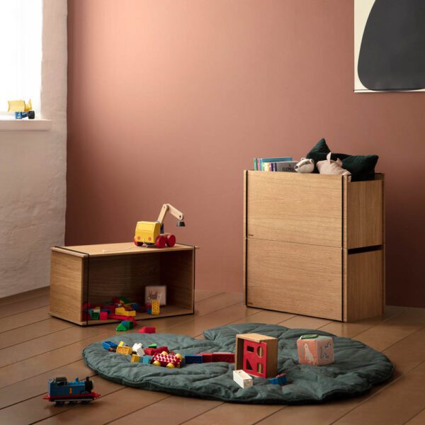 Natural light, perspective view, editorial style photo of rectangular wooden storage boxes and toys splattered across a green, circle-shaped rug.