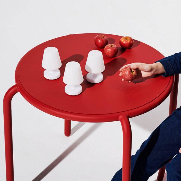 A man is holding an apple with 3 apples on the red table next to Edison the mini table lamp.