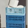 A stack of colour crate storage box in shades of blue with toilet rolls inside the box