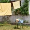 Yellow bedsheet is drying in the backyard and Hay washing laundry basket on a chair