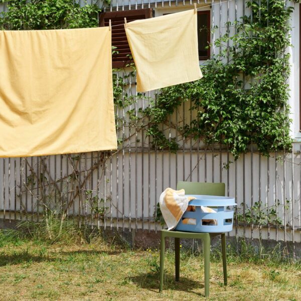 Yellow bedsheet is drying in the backyard and Hay washing laundry basket on a chair