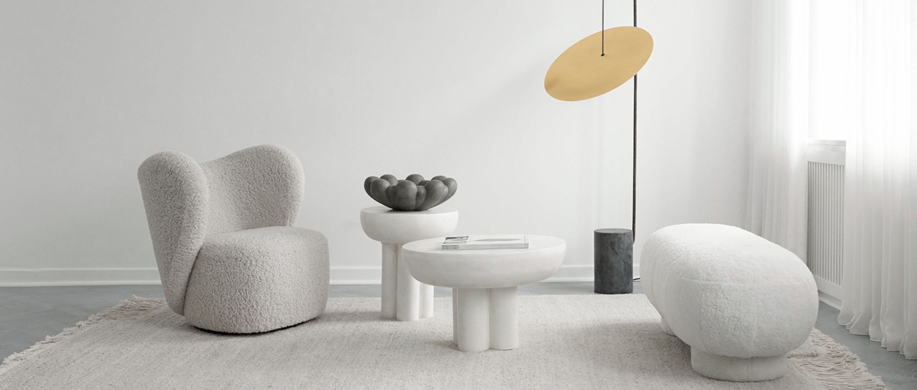 A styled shot of products from 101 COPENHAGEN, including lighting, furniture, and decor. The highlight piece is the large Bloom Tray, which sits on a table. It contrasts the mainly white setting with its black colouring and unique flower-like silhouette.