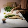 A woman is chopping the vegetable on a wooden board with kitchen timer on a marble bench.