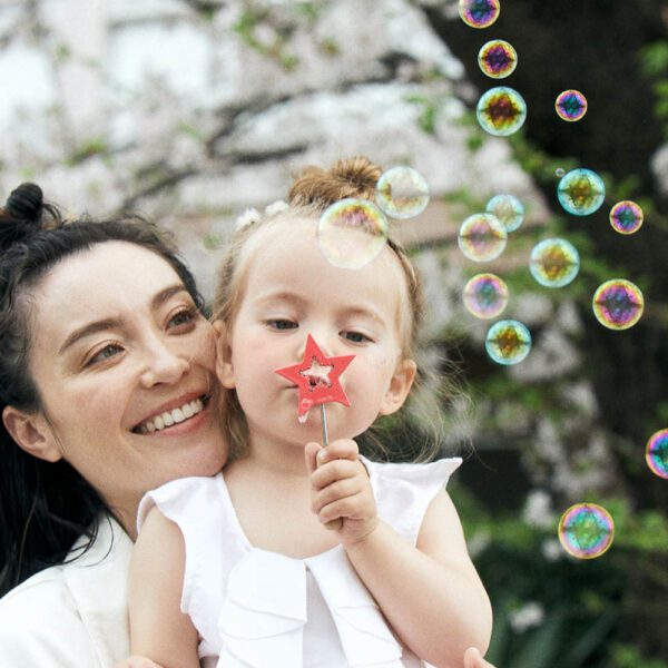 A toddler is blowing magical bubble wands with her mother at the park.