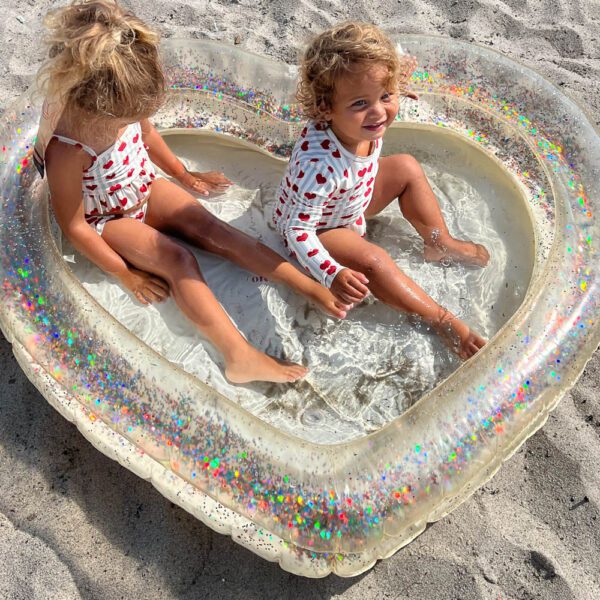 Two kids are playing in the heart shaped kids indoor and outdoor pool with glitter and confetti at the beach.