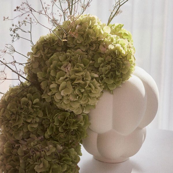 Uva vase with green flowers on a table.