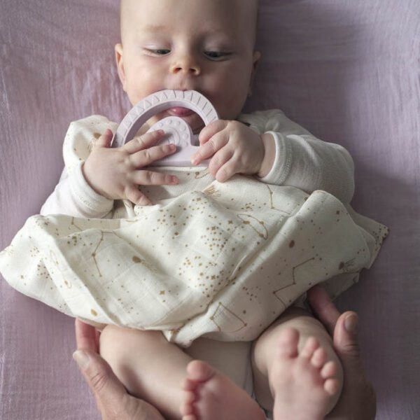 A baby is holding a natural rubber teether rainbow in lilac.