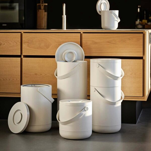 A kitchen with four, different sized, cylindrical trash bins on the floor.