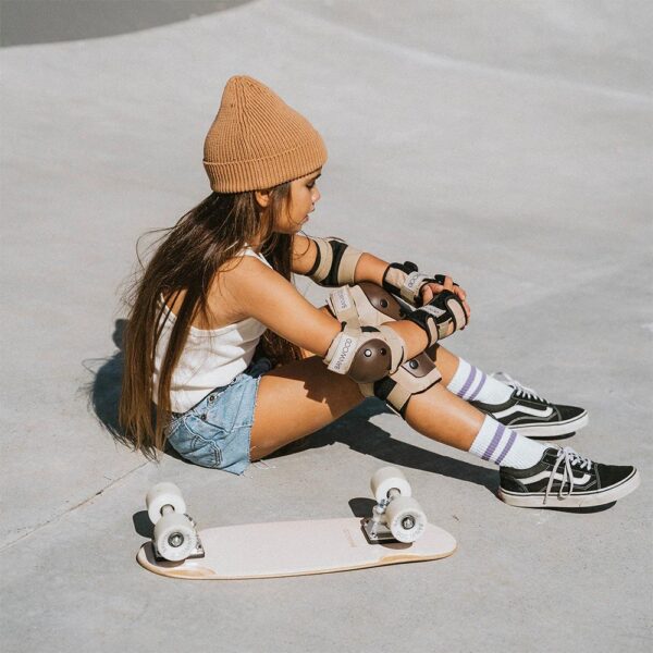 A child sitting inside a skate park next to a flipped skateboard and complete with protective gear.