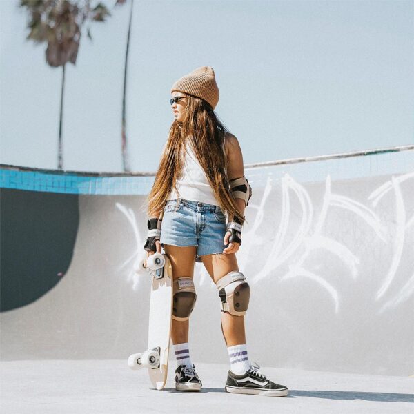 A child standing inside a skate park's bowl holding a skateboard and complete with protective gear.