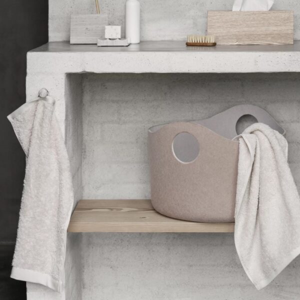 A felt basket placed under a bathroom sink next to hand towels.