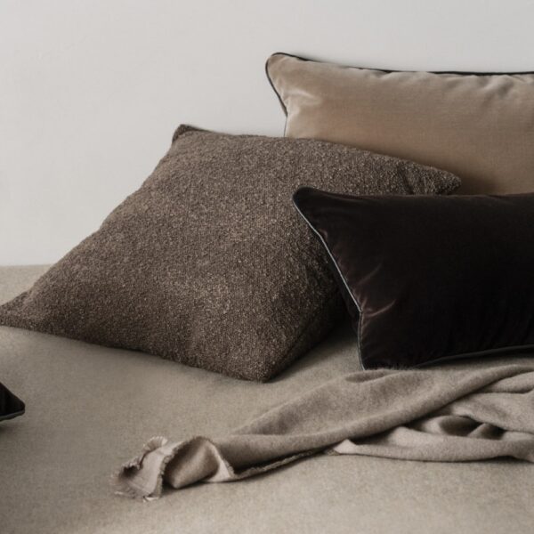 A stack of square shaped velvet cushions next to a blanket.