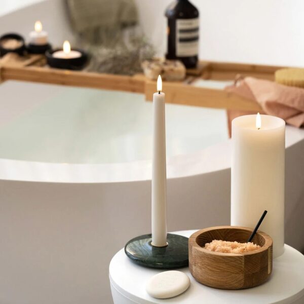 An oval-shaped, flameless candle remote controller placed next to different shaped and sized candles.