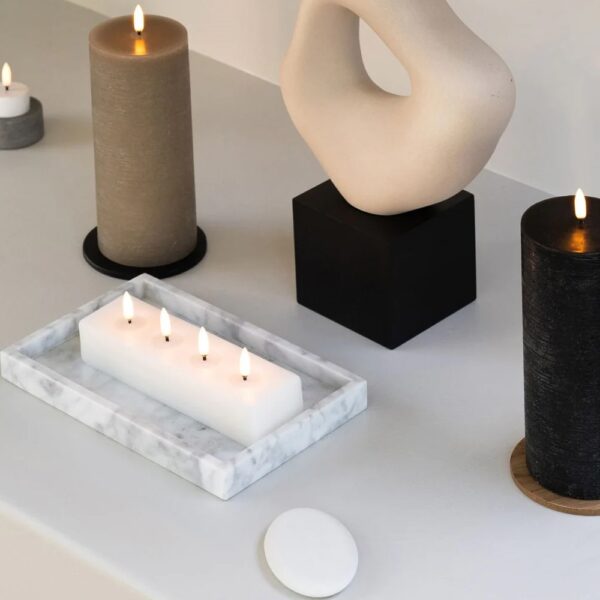 A rectangular-shaped flameless candle next to a remote controller and different shaped flameless candles.