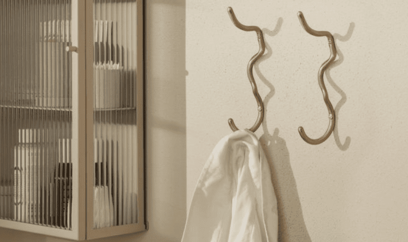 Two ferm LIVING Curvature hooks installed on a bathroom wall. One is empty but the other is holding a towel.